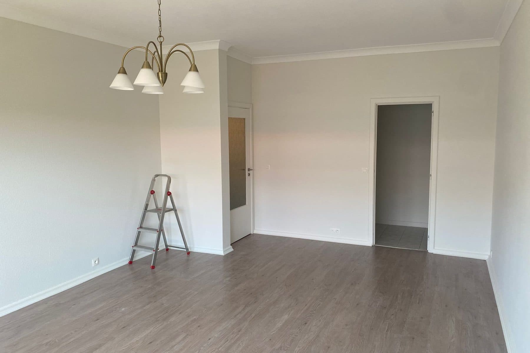 Pièce d’appartement fraîchement repeinte, sol gris, escabeau et lustre en laiton