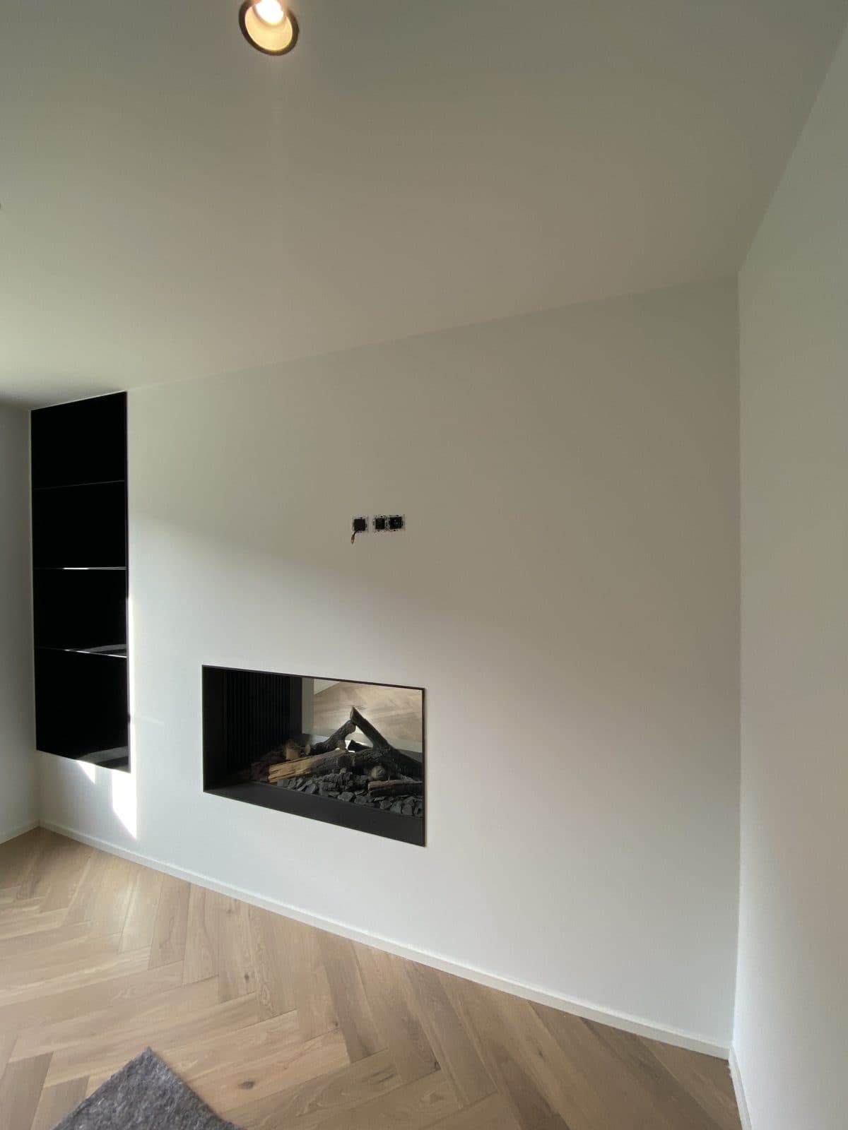 Mur blanc avec foyer traversant et niche noire, parquet en chêne clair à bâtons rompus
