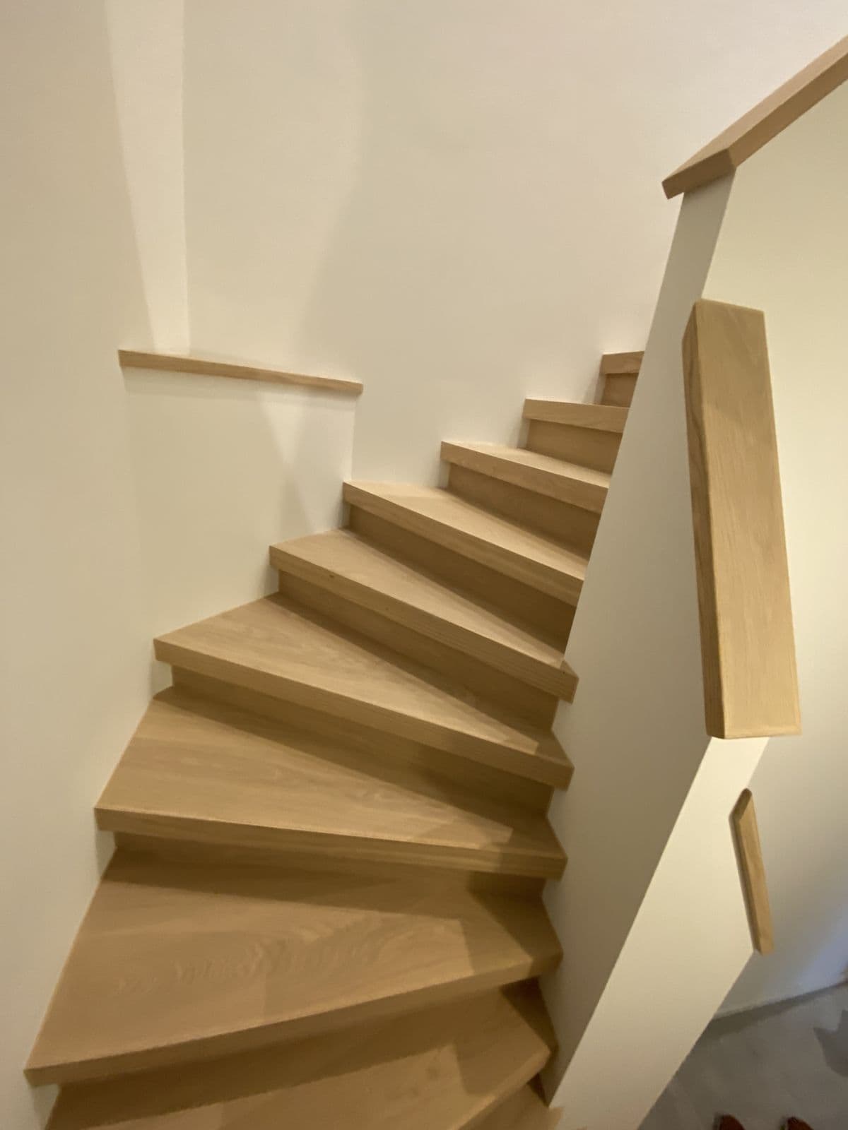 Escalier tournant habillé de chêne, main courante en chêne sur un mur blanc