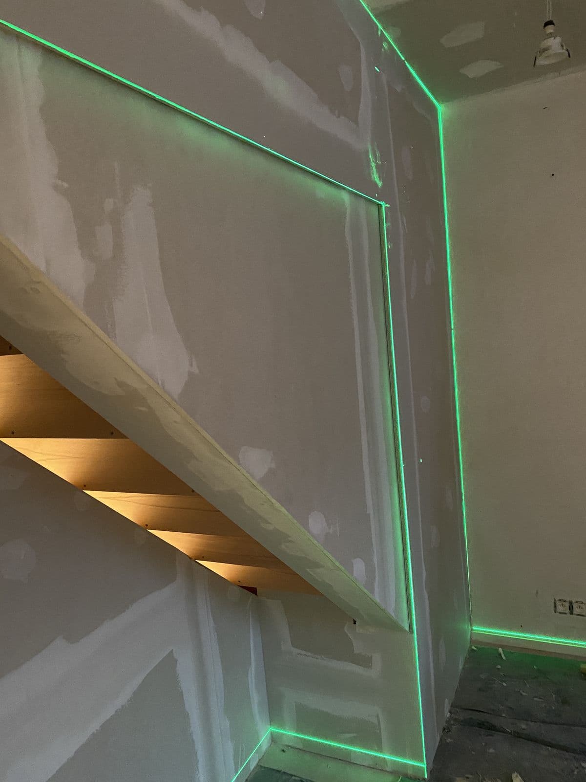 Escalier en cours : marches en chêne éclairées par-dessous, lignes vertes du laser sur les murs en plâtre