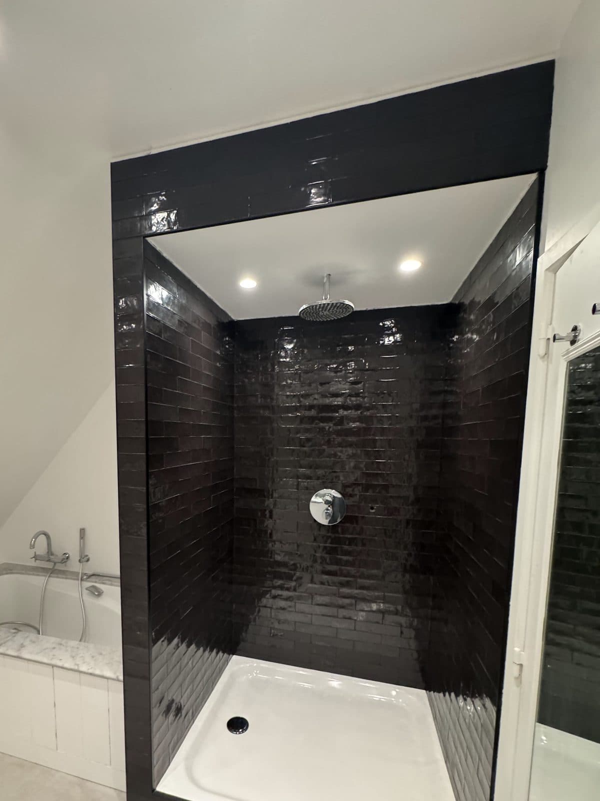 Douche en alcôve, carreaux métro noirs brillants, pomme de pluie et receveur blanc