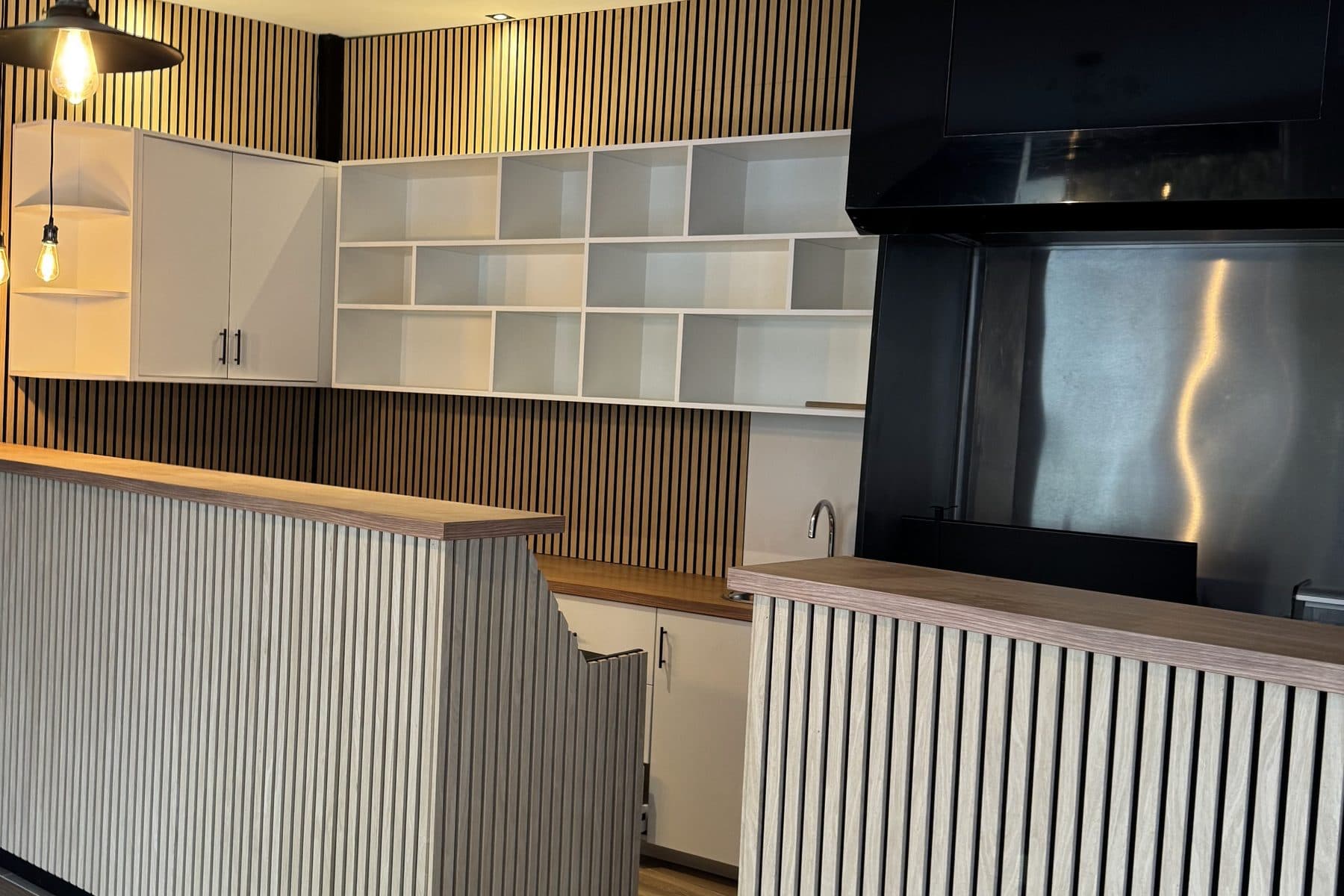 Bar à façade en lattes verticales et plan en chêne, casiers blancs et hotte noire