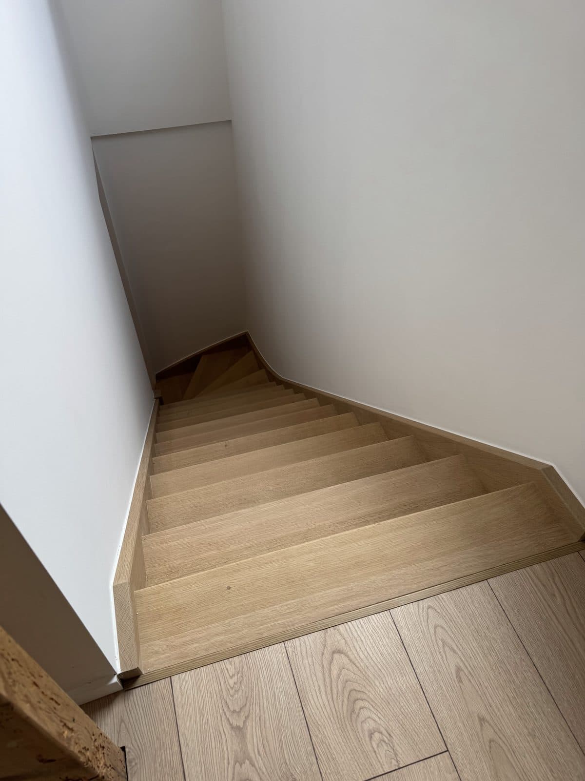 L’escalier vu d’en haut, marches aspect chêne entre deux murs blancs