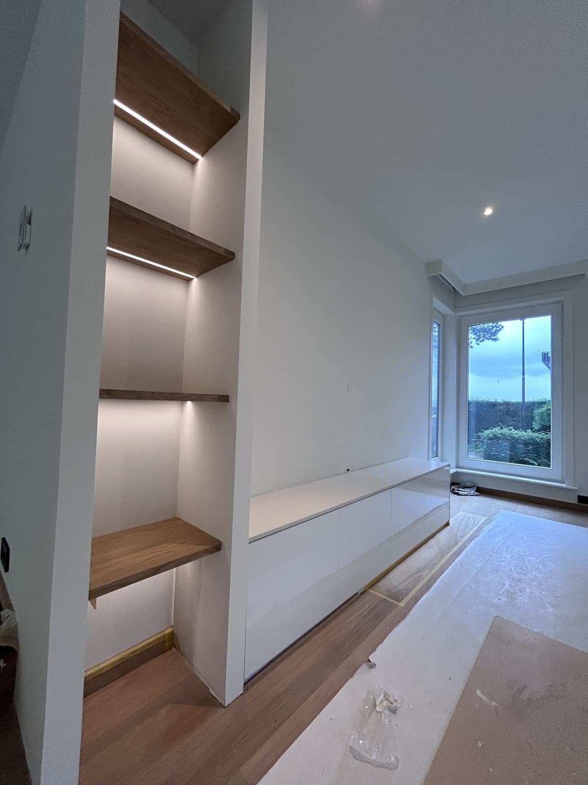 Niche aux étagères en chêne éclairées, long meuble bas blanc, porte vers le jardin