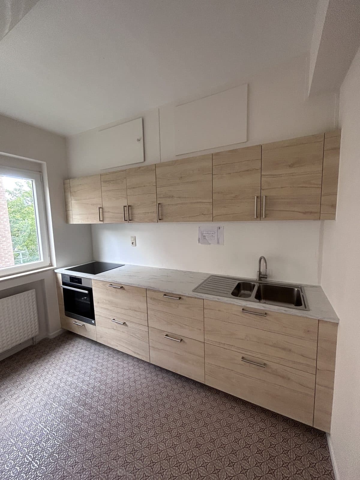 Cuisine en ligne sous la pente : façades aspect chêne clair, plan aspect marbre, carreaux à motifs au sol