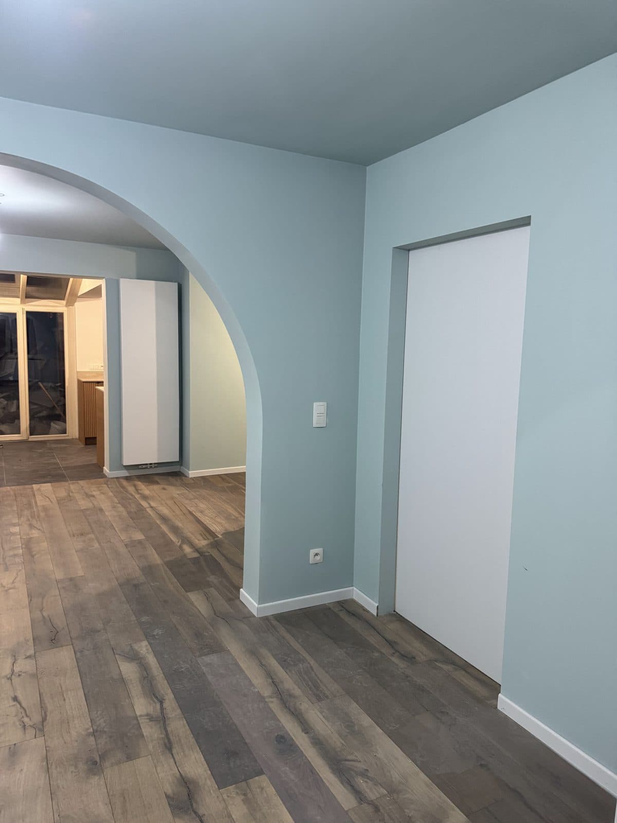 Arche à gauche, murs bleu pâle, porte blanche affleurante, véranda au fond
