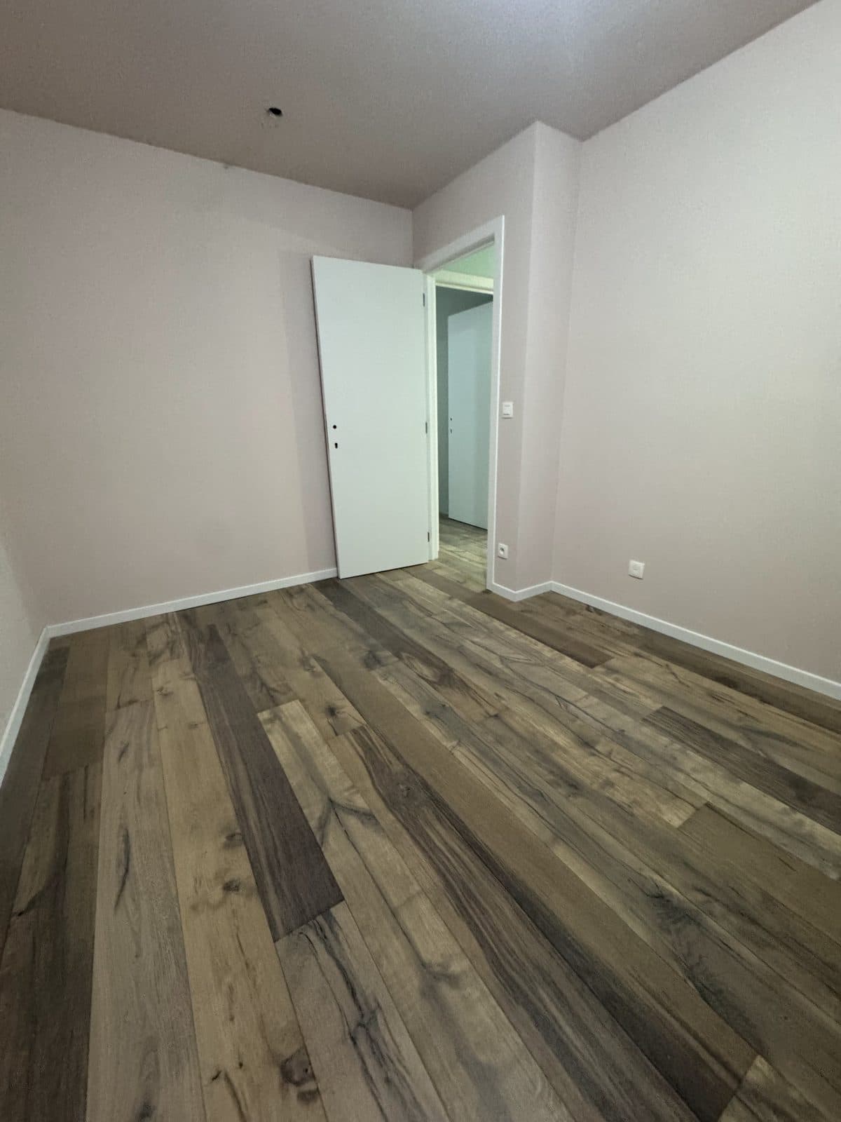 Chambre rose pâle, porte blanche ouverte, parquet en chêne foncé