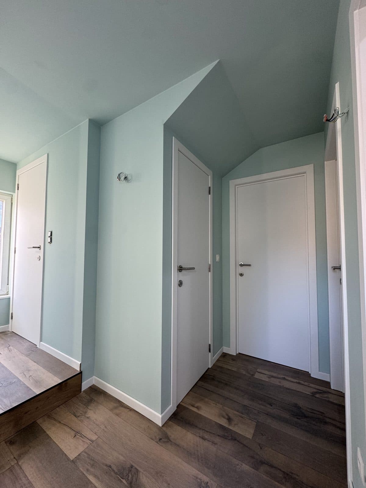 Couloir vert menthe sous la pente, portes blanches et marche en chêne