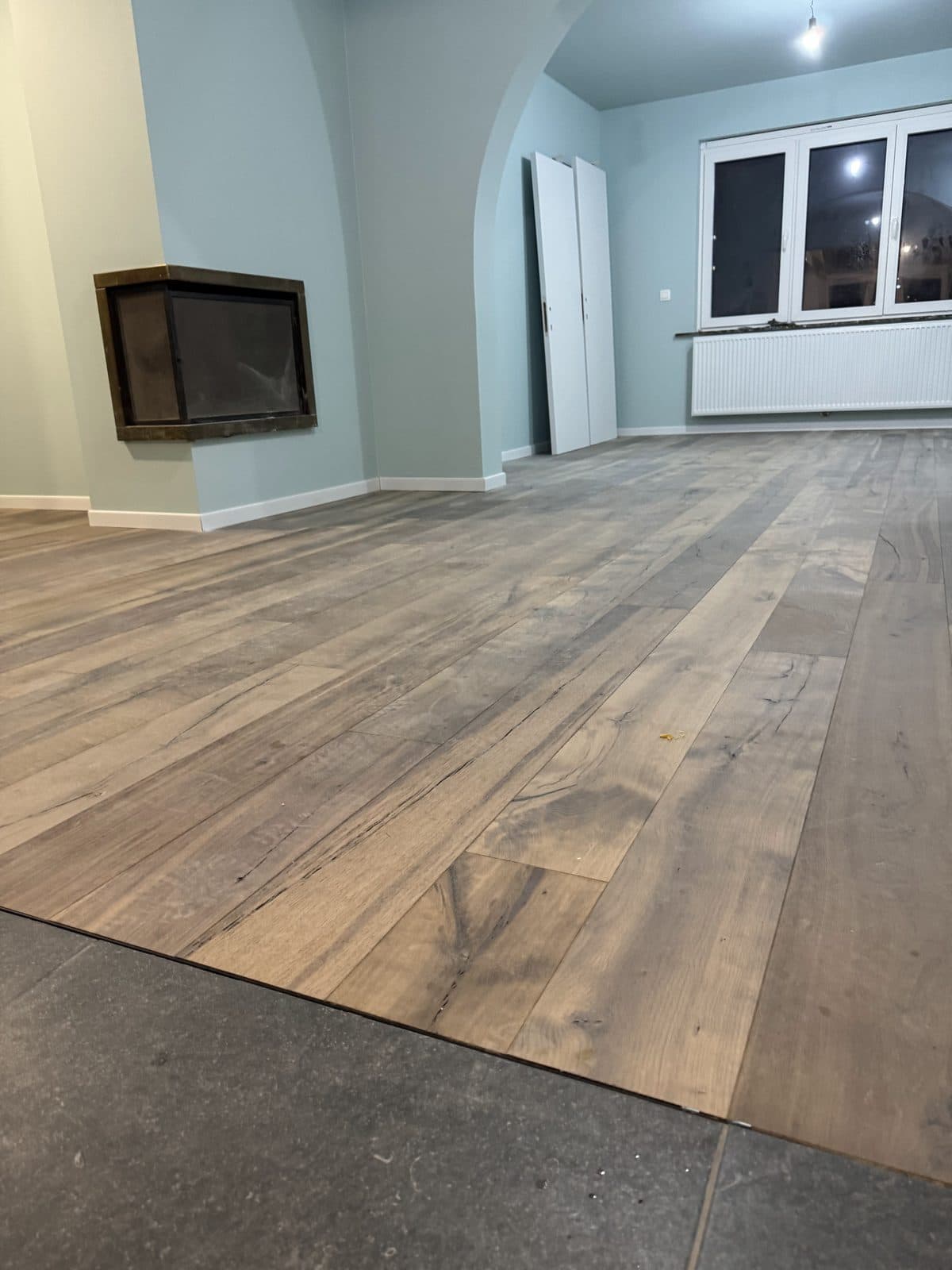 Parquet en chêne rustique vu au ras du sol, insert de cheminée en angle, portes posées contre le mur