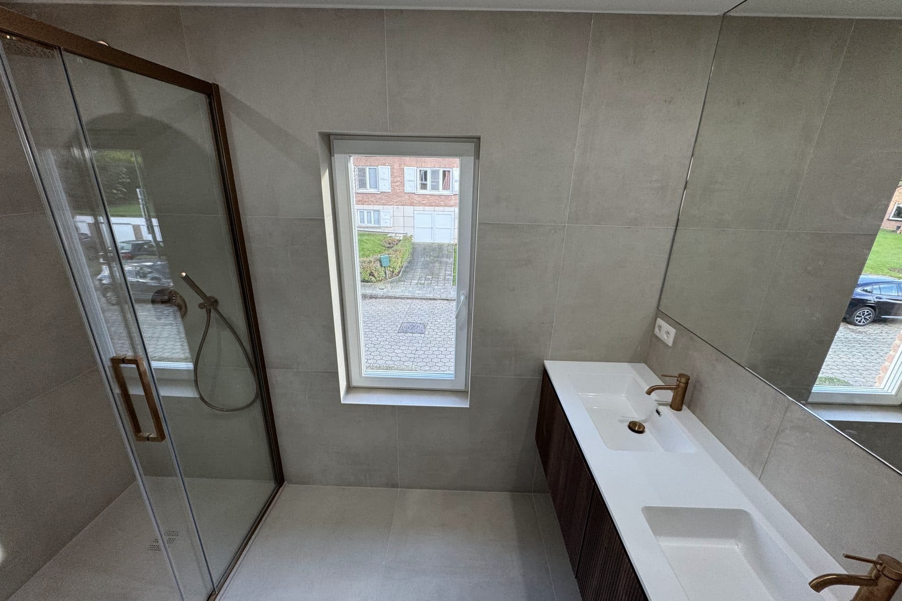 Grands carreaux gris, porte de douche coulissante à cadre bronze, long plan vasque blanc sur bois cannelé sombre