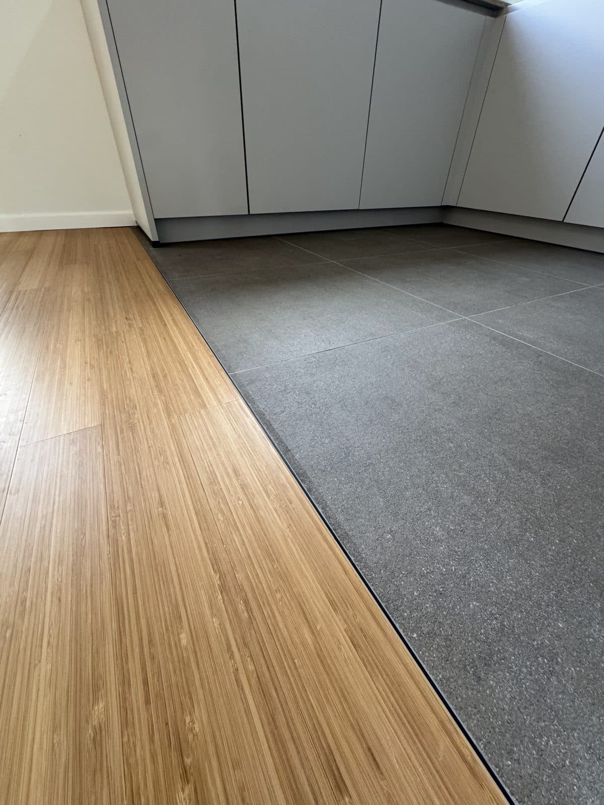 Jonction du parquet et du carrelage en pierre gris foncé, devant des meubles blancs sans poignées