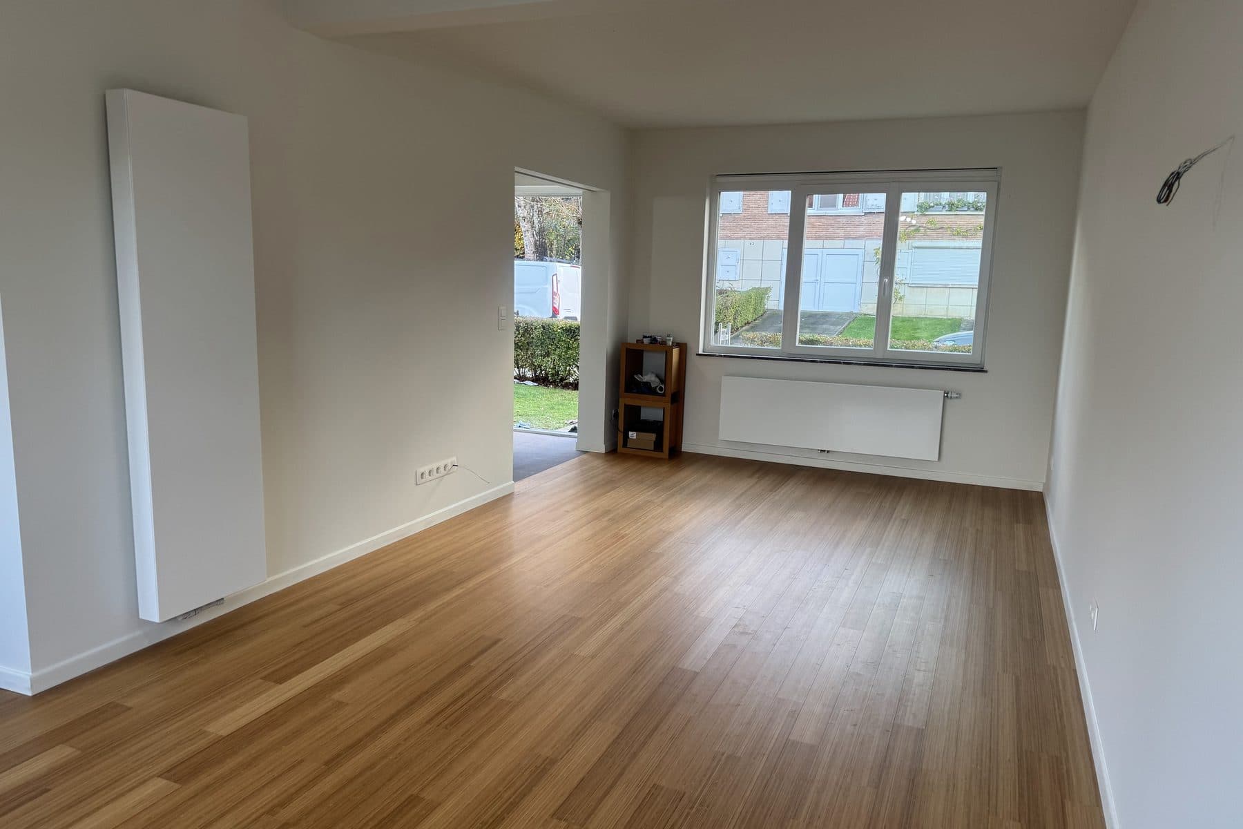 Pièce vide au parquet à lames fines, ton bambou, haut radiateur vertical blanc et fenêtre à trois vantaux