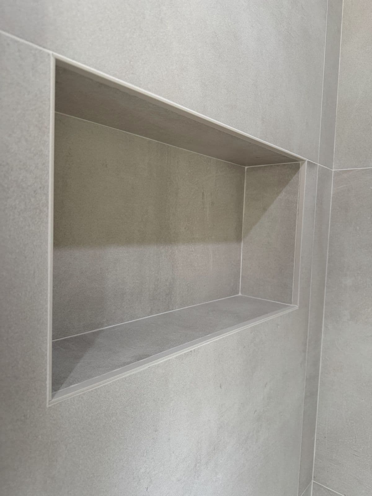 Niche carrelée dans la douche, grands carreaux gris clair, angles nets
