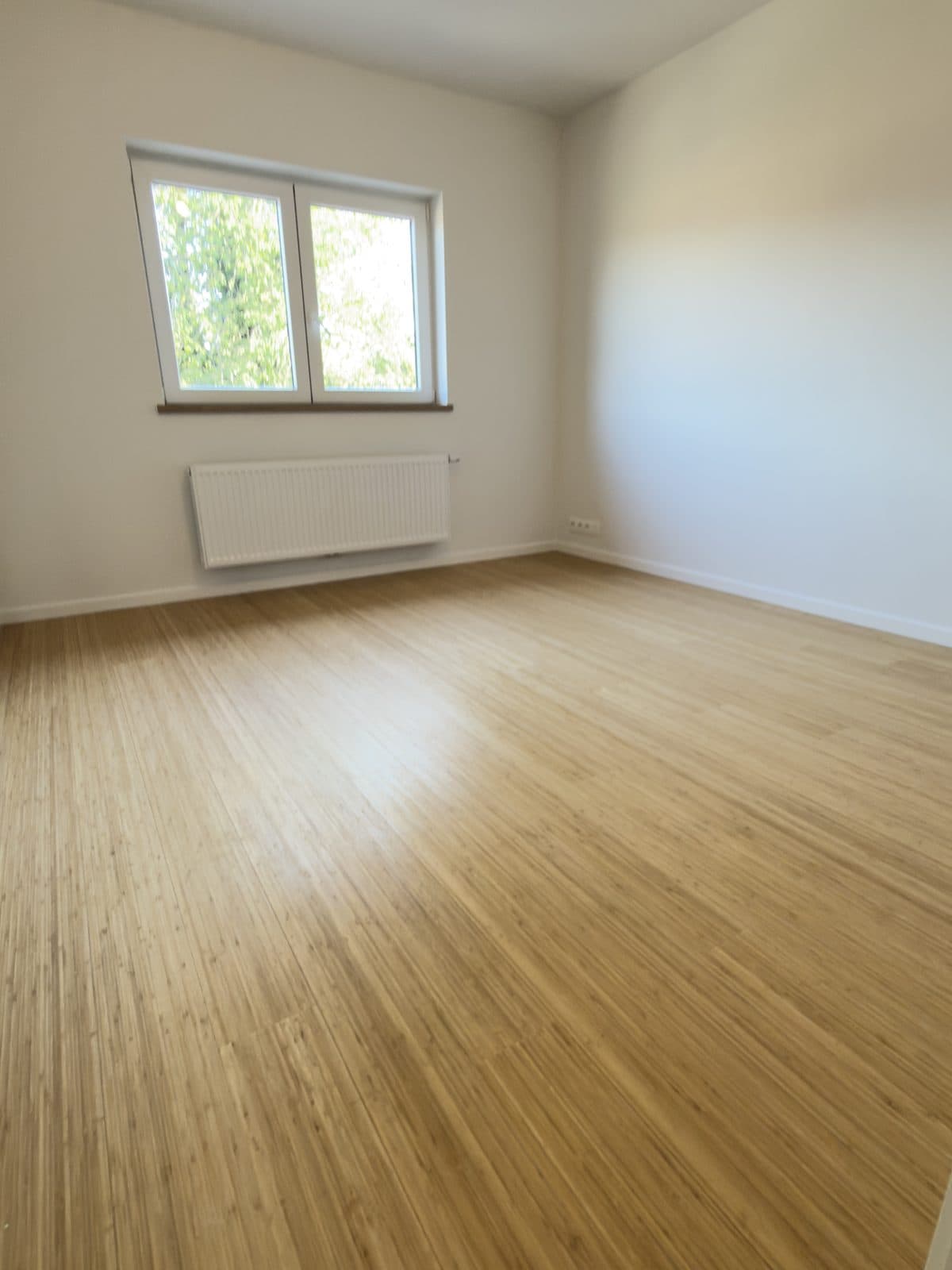 Parquet à lames fines dans une chambre, fenêtre à deux vantaux et radiateur