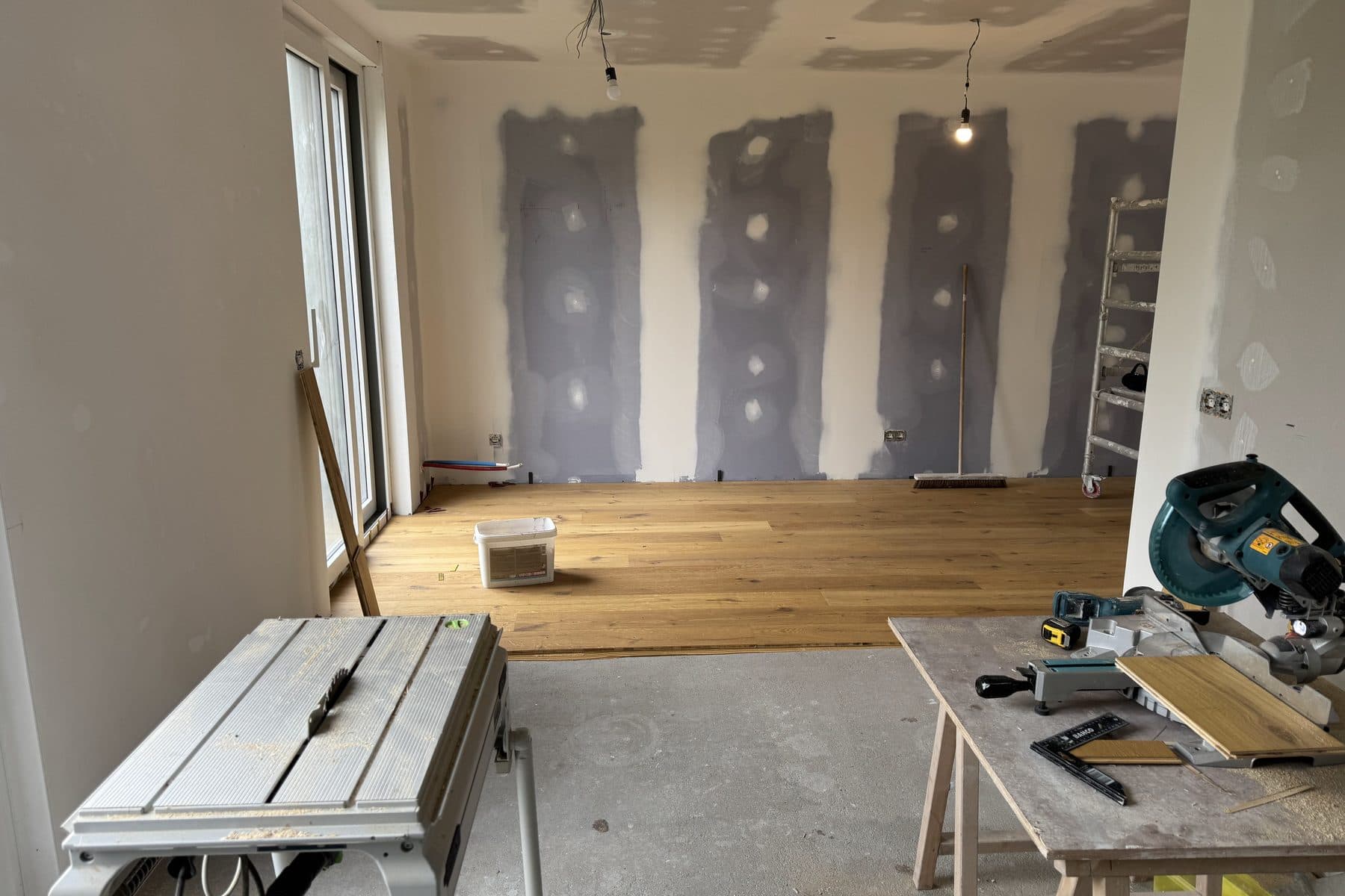 Murs en plaques de plâtre aux joints enduits, parquet en chêne posé au fond, scie sur table et scie à onglet au premier plan