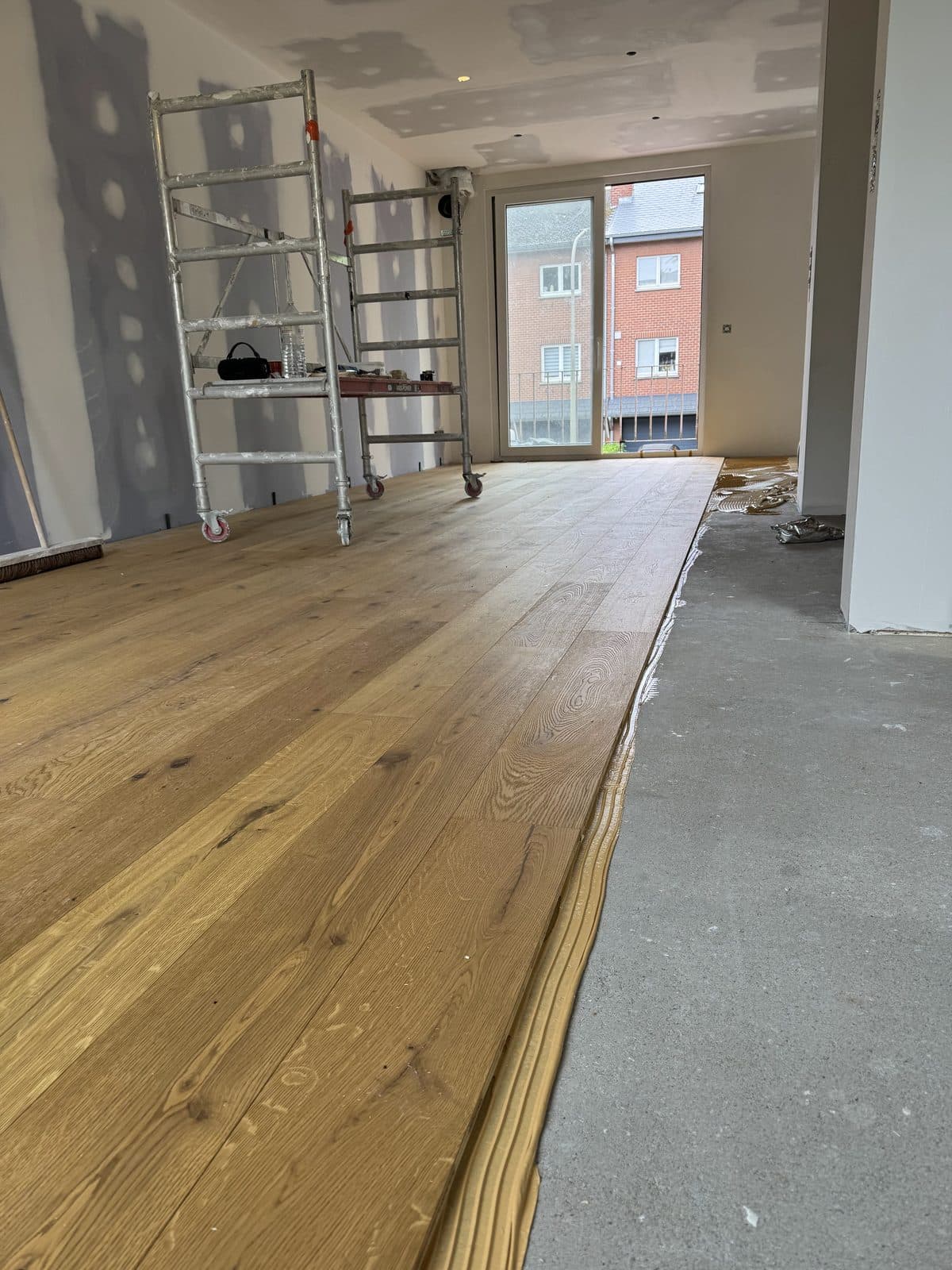 Parquet en chêne posé sur toute la longueur de la pièce, échafaudages roulants et porte-fenêtre côté rue