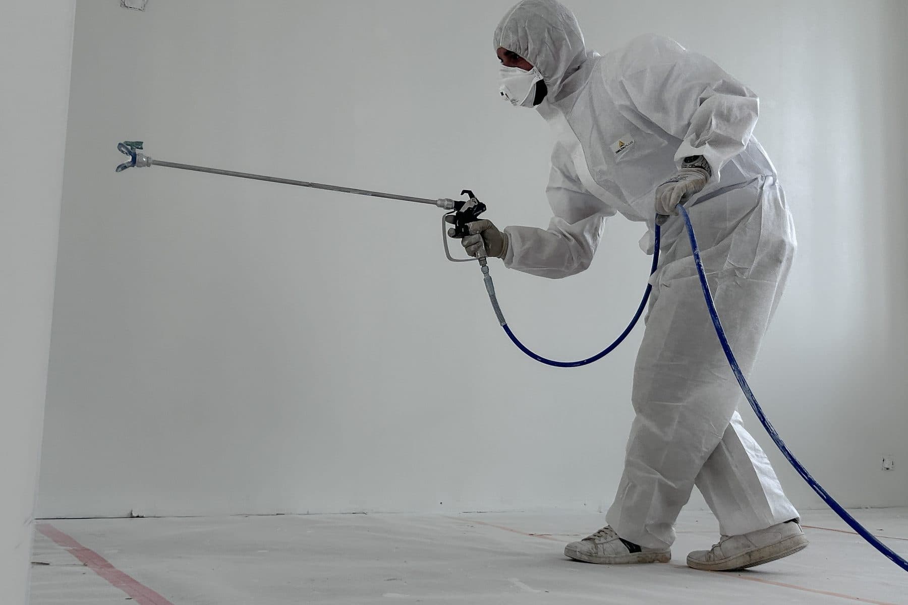 Un peintre en combinaison et masque applique la peinture au pistolet, lance à rallonge
