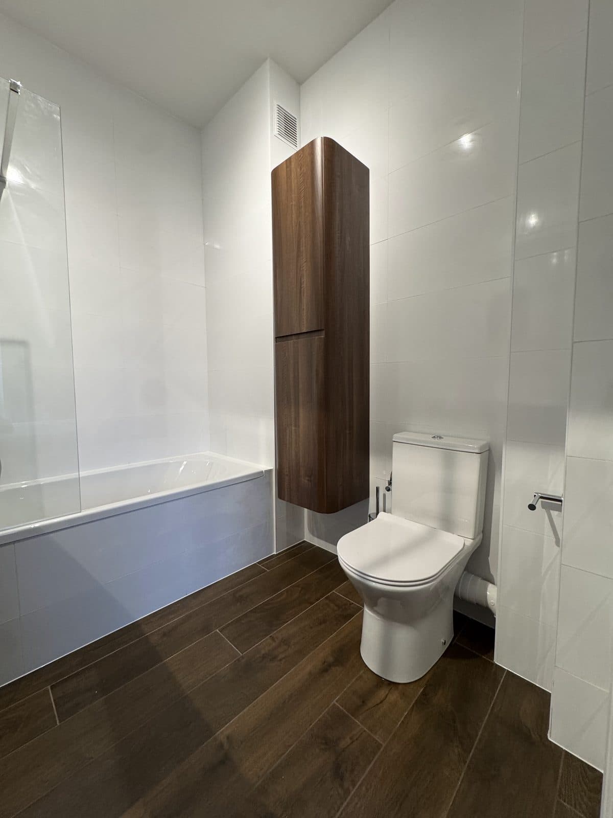 La même salle de bain : baignoire, colonne en bois sombre et WC