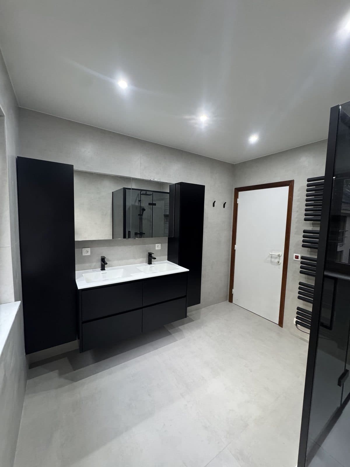 Double vasque noire et colonnes noires, armoire miroir, carrelage gris, sèche-serviettes noir