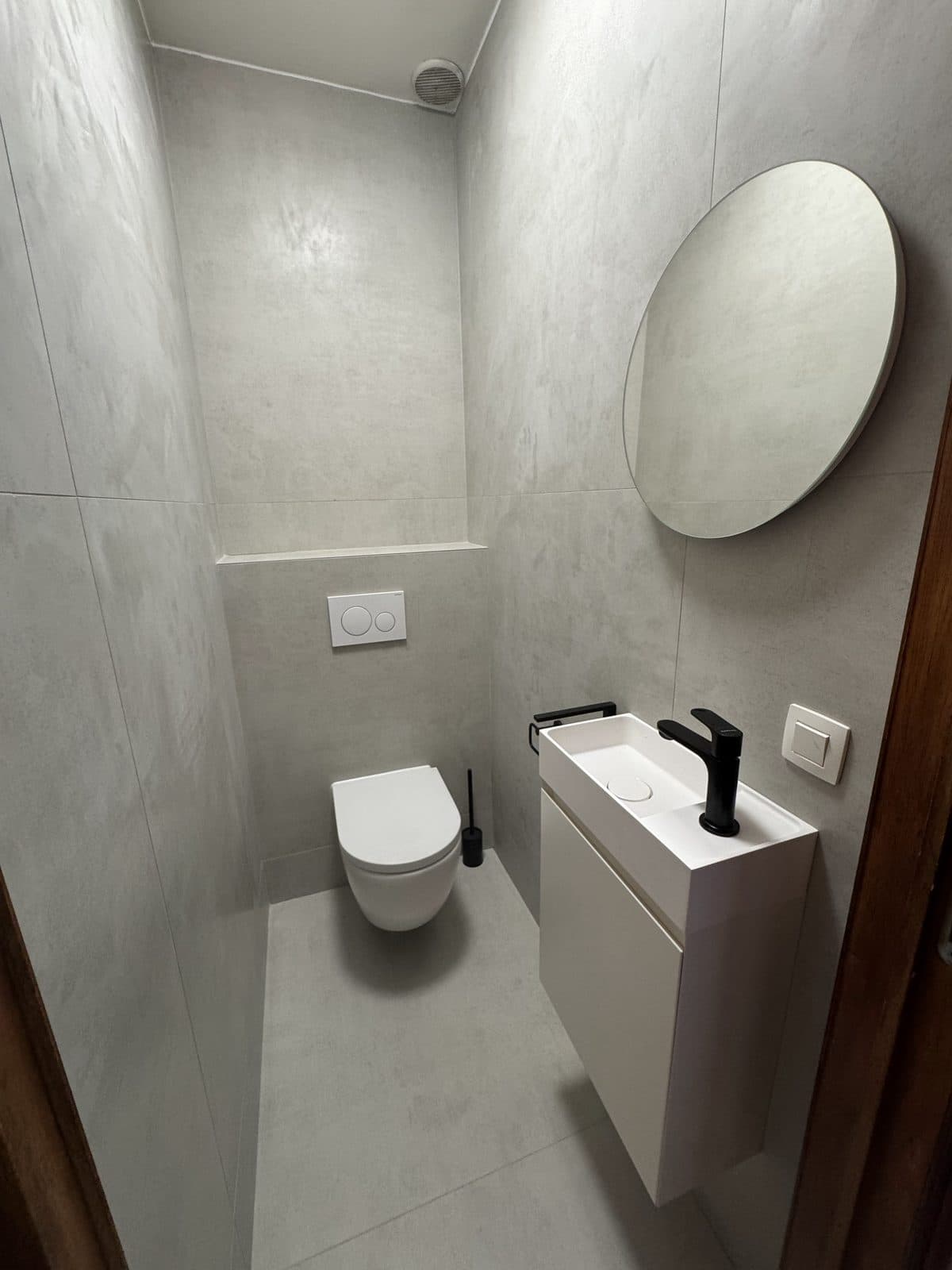 WC : grands carreaux gris, miroir rond, petit meuble vasque blanc à robinet noir