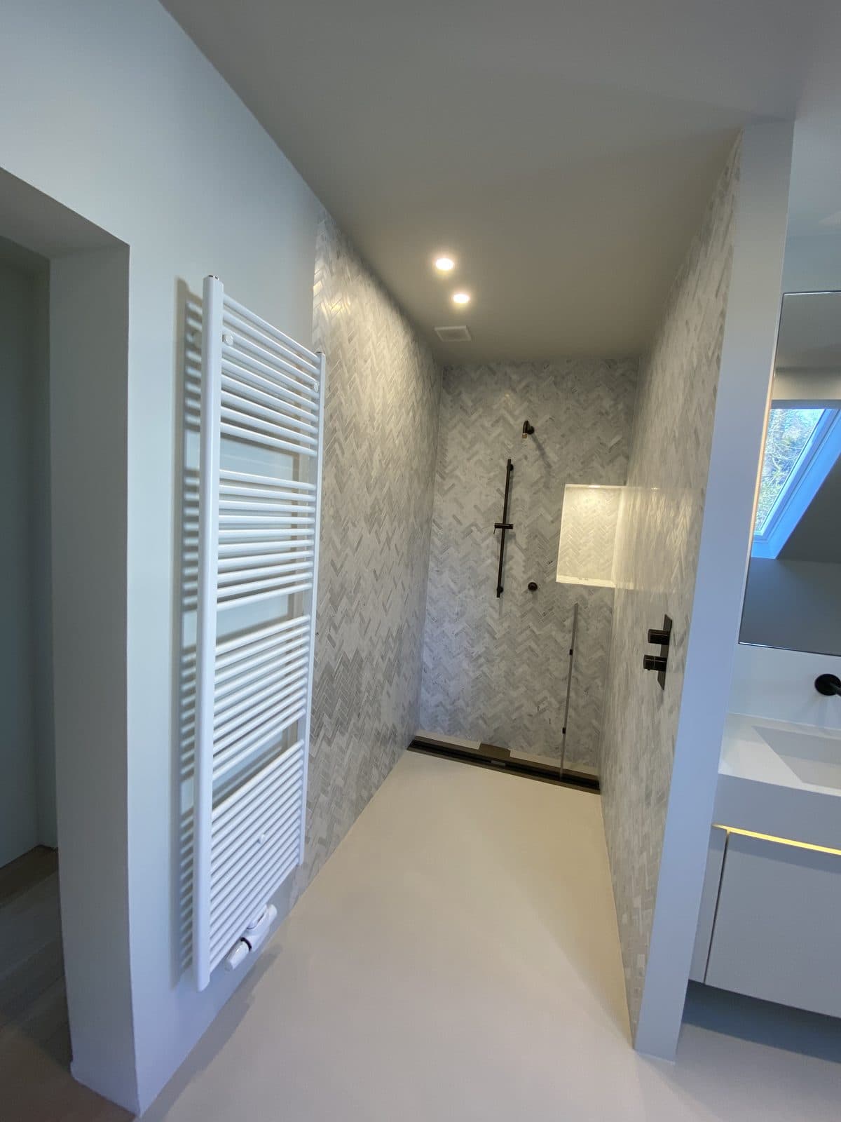 Sèche-serviettes blanc sur une cloison, douche en mosaïque de marbre au fond, robinetterie noire