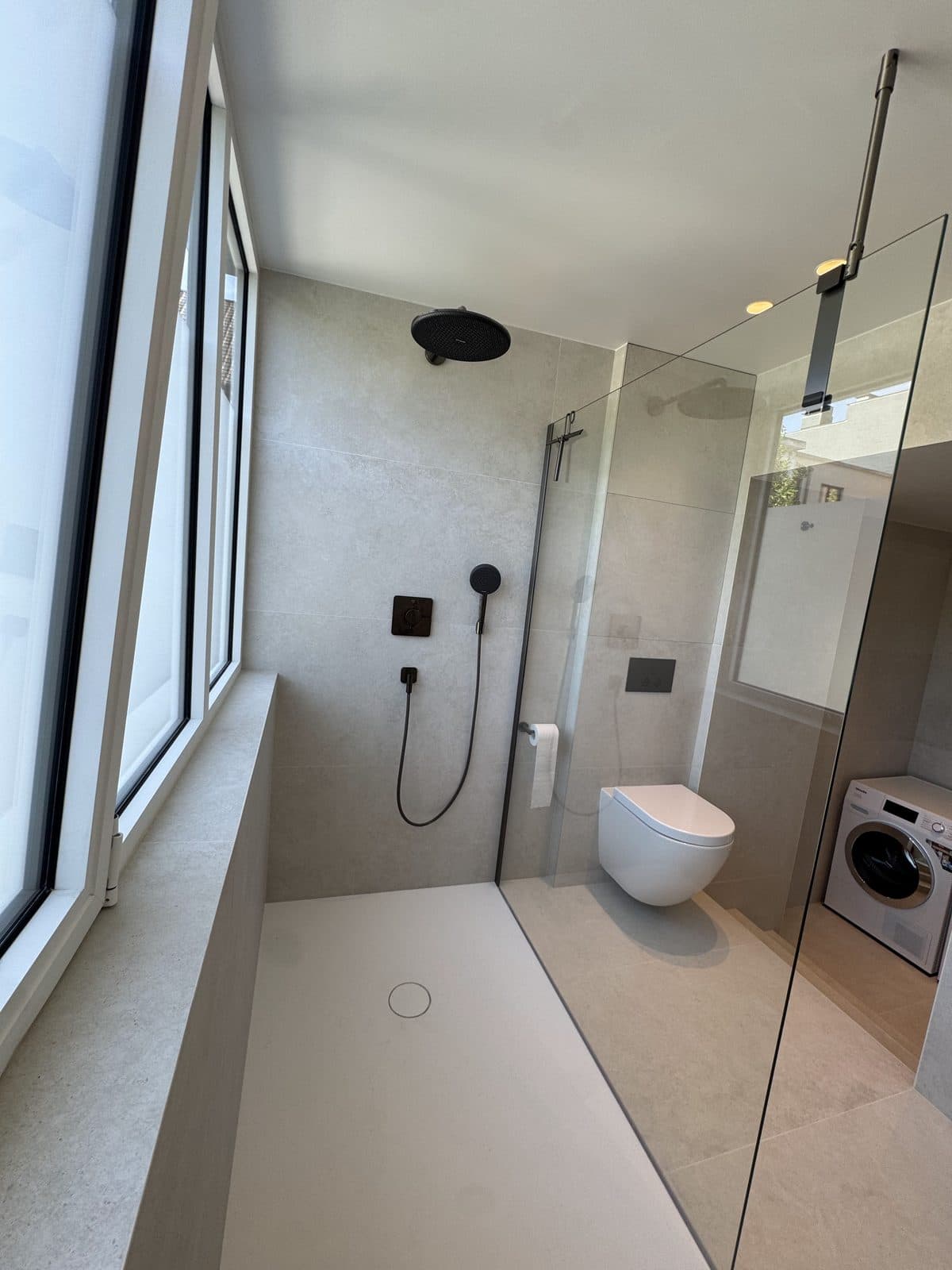La douche vue depuis la fenêtre : pomme de pluie noire, paroi vitrée, WC suspendu