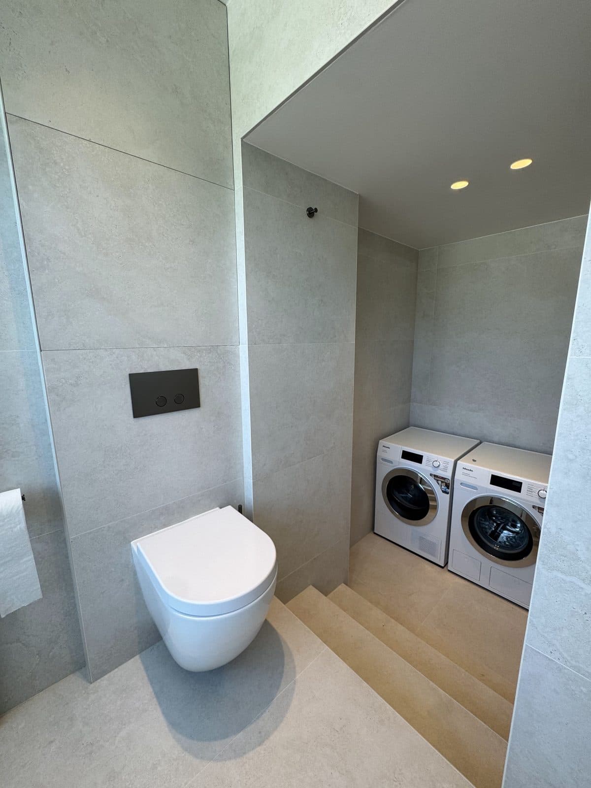 WC suspendu à plaque noire, lave-linge et sèche-linge sur une marche, dans une niche