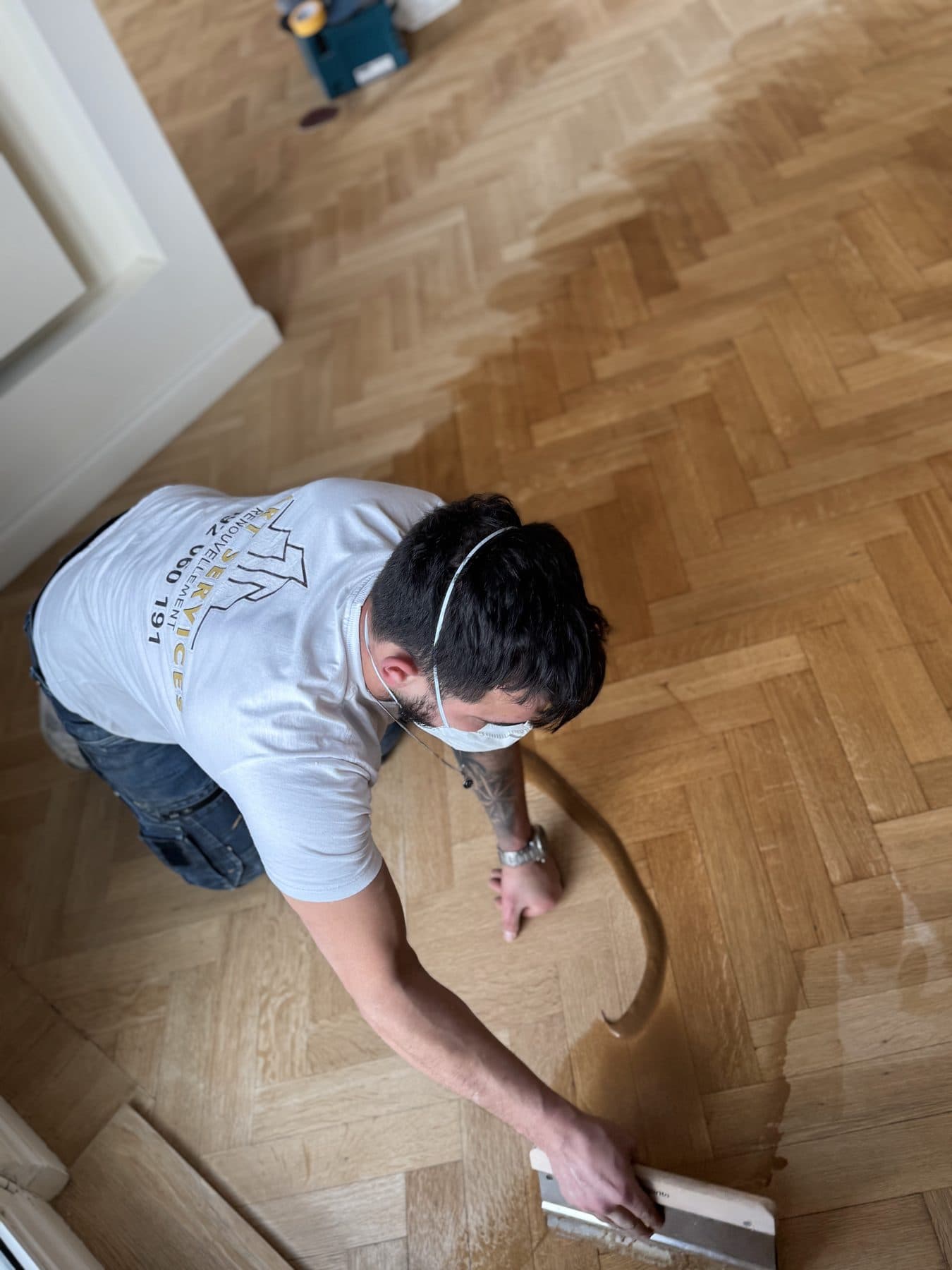 Application de la finition à la spatule large sur un parquet à bâtons rompus