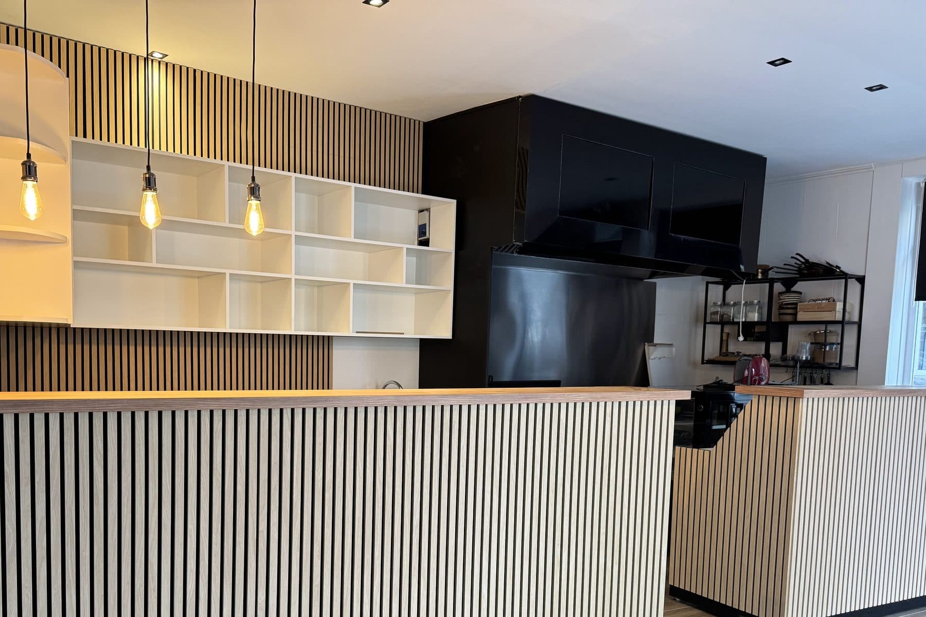 Bar vu de face : façade en lattes verticales claires, plan en chêne, trois suspensions à ampoule nue