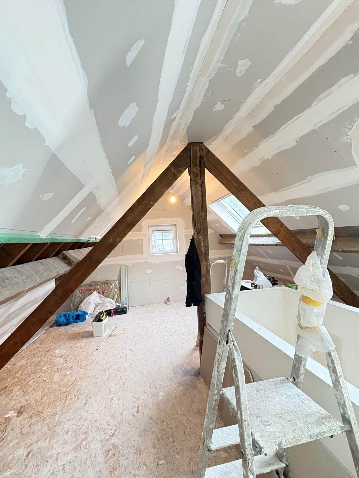 Placas de drywall com as juntas tratadas sob as tesouras, escada de abrir perto do vão