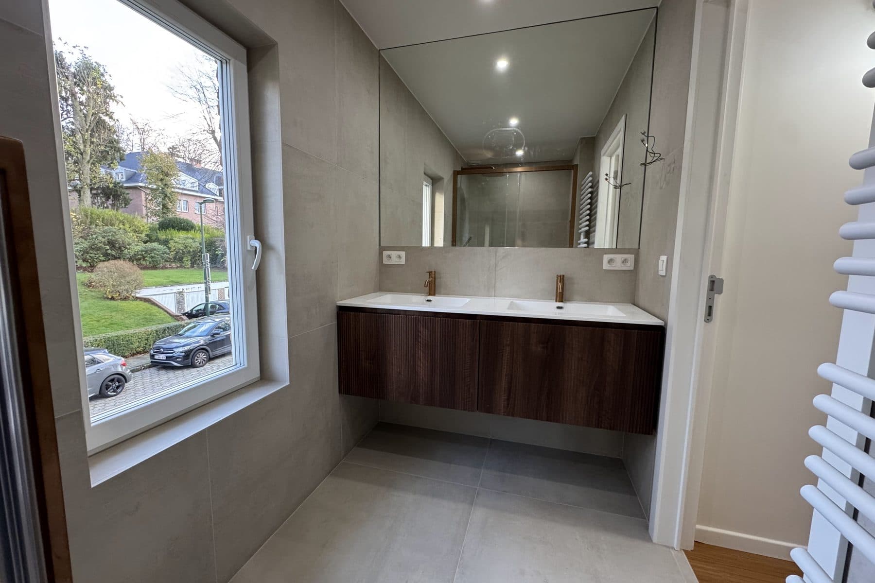 Salle de bain : double vasque sur meuble cannelé sombre, robinetterie cuivrée, grand miroir, sèche-serviettes blanc
