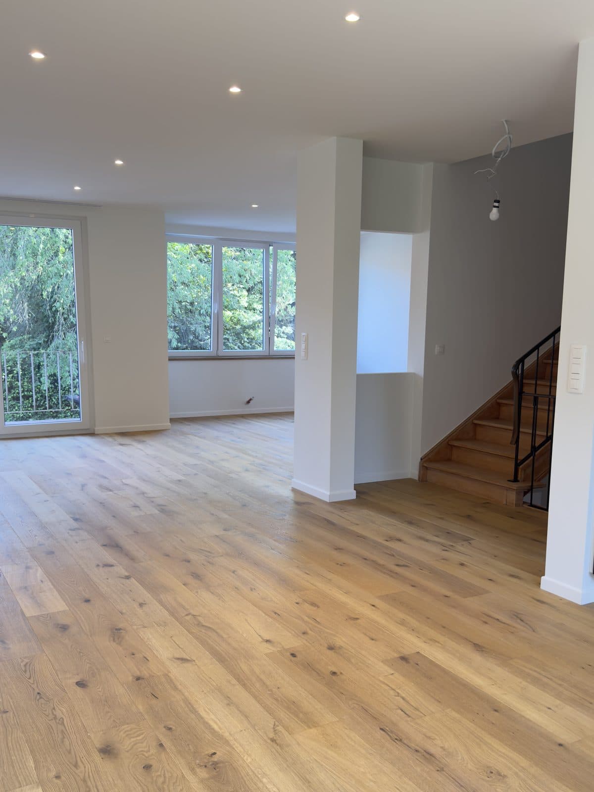 Séjour terminé : parquet en chêne rustique, escalier à droite et grande fenêtre en trois parties au fond