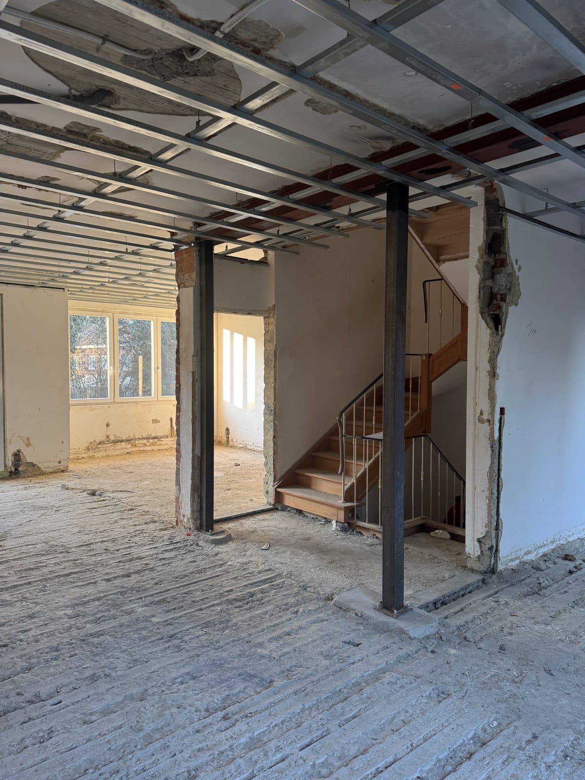 Niveau mis à nu : deux poteaux en acier, escalier en bois à droite et fenêtre en trois parties au fond