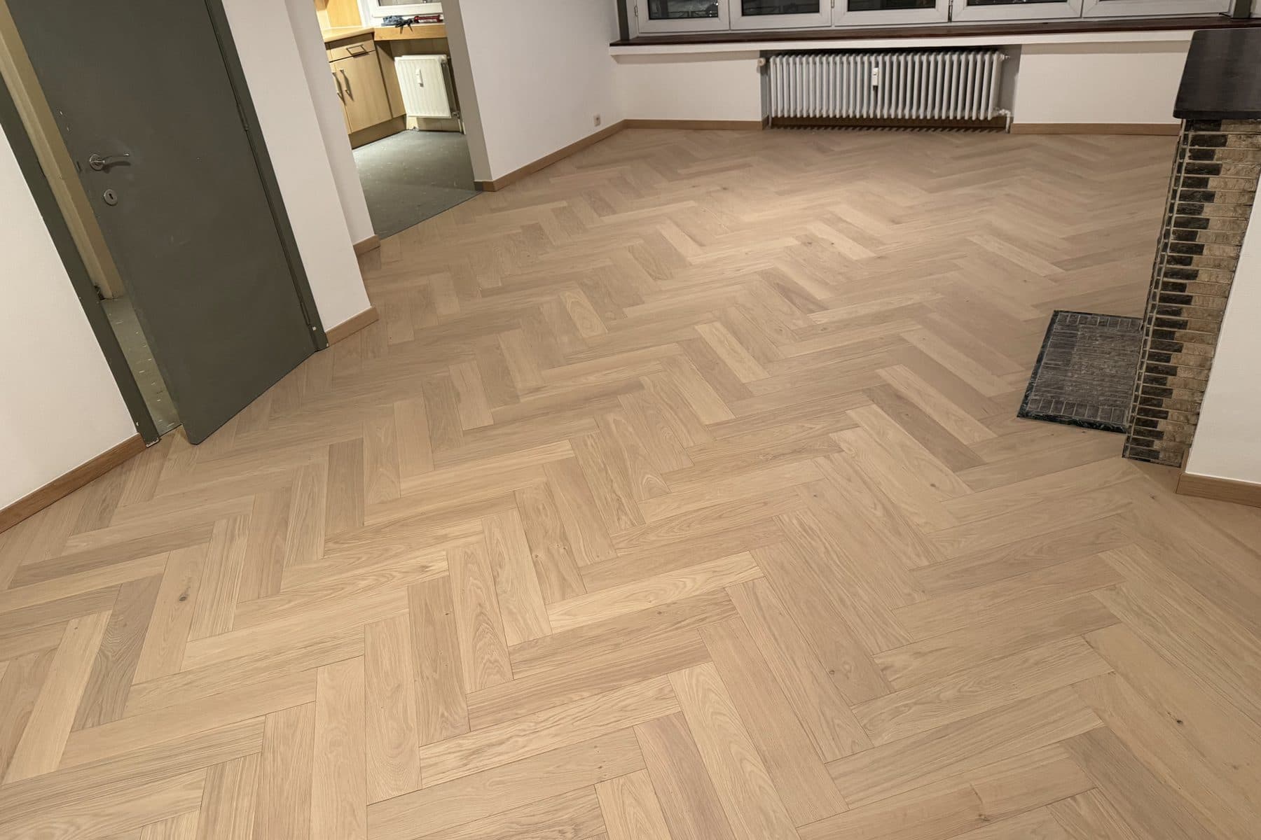 Parquet en chêne clair à bâtons rompus terminé, porte vert foncé à gauche, fenêtre à cinq vantaux et radiateur