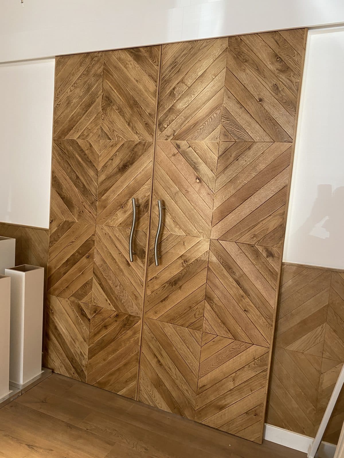 Portes coulissantes en chêne à chevrons fermées, poignées en barre d’acier cintrée, soubassement en chêne