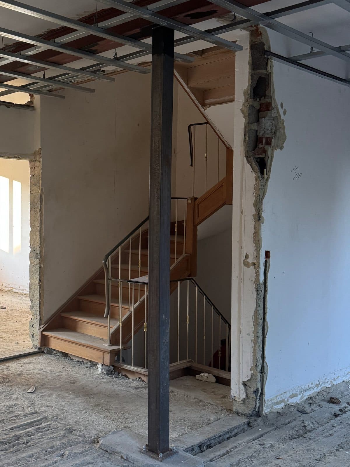 Escalier en bois à rampe métallique dans un niveau mis à nu, poteau en acier au premier plan