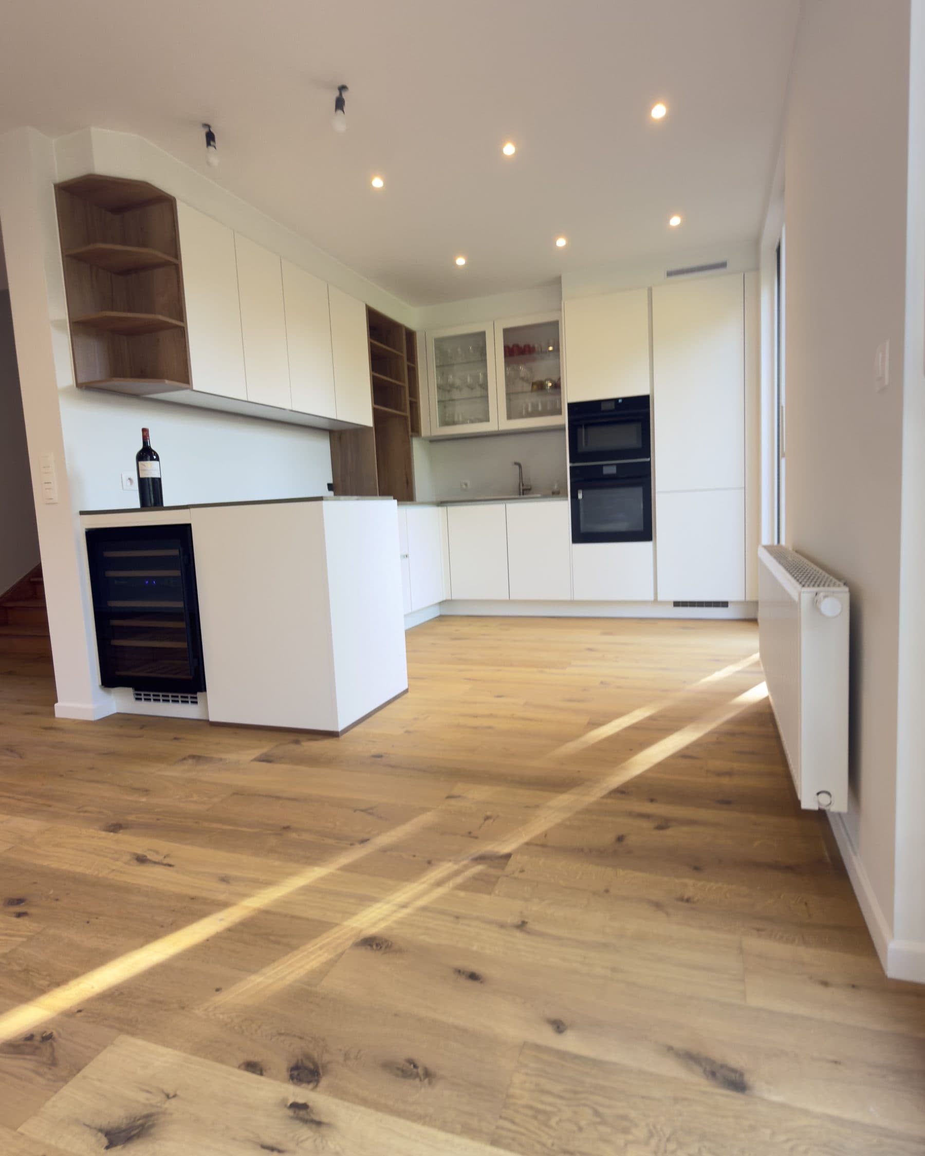Cuisine blanche ouverte sur le séjour, niches en chêne et parquet en chêne, dans une maison entièrement rénovée